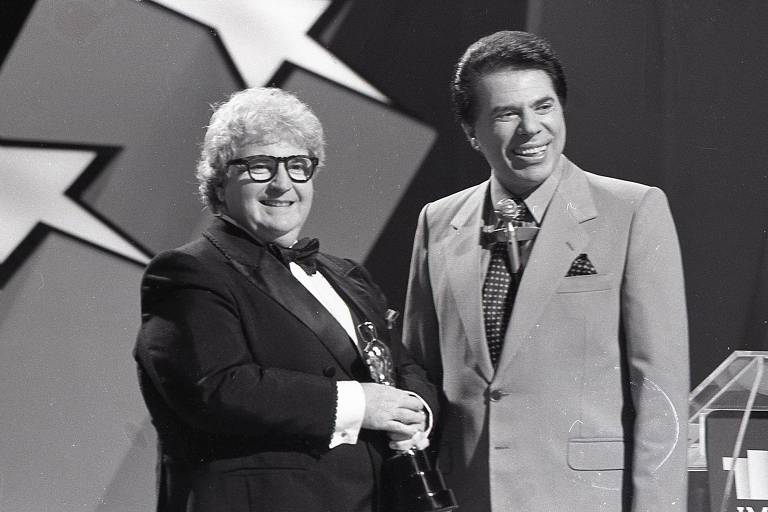 &ocirc; Soares ajustando seus &oacute;culos redondos coloridos enquanto sorri de canto.