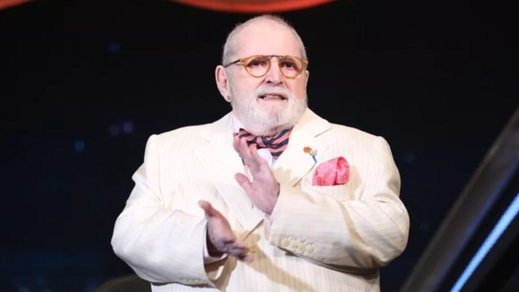 &ocirc; Soares ajustando seus &oacute;culos redondos coloridos enquanto sorri de canto.