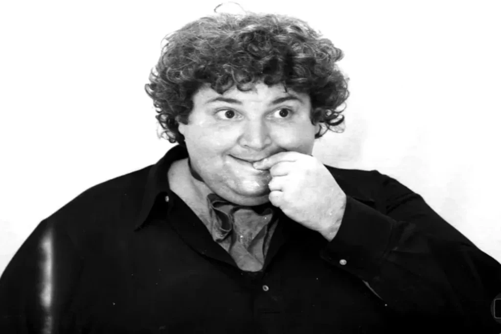 &ocirc; Soares ajustando seus &oacute;culos redondos coloridos enquanto sorri de canto.