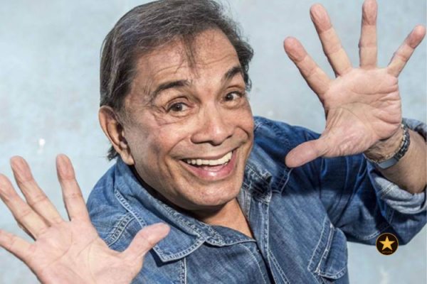 Dedé Santana sentado em um camarim de circo, em frente a um espelho com lâmpadas amareladas.