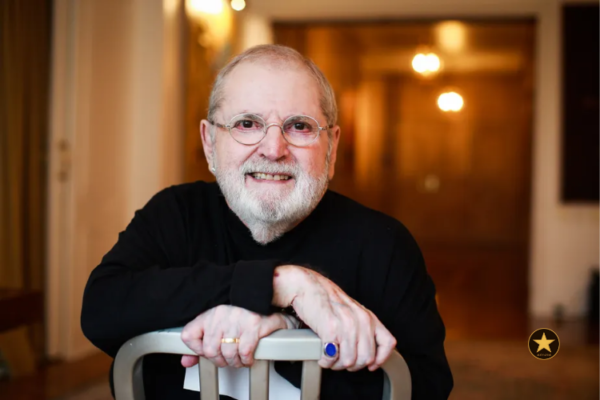 ô Soares ajustando seus óculos redondos coloridos enquanto sorri de canto.